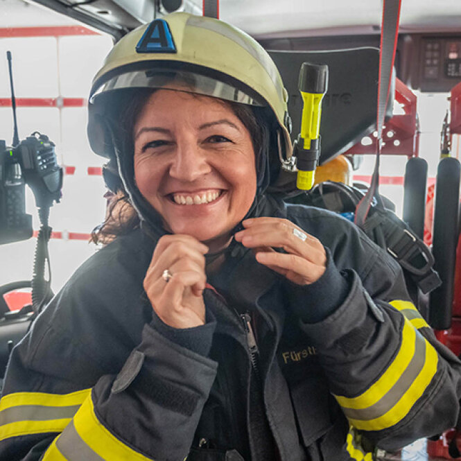 Porträtfoto: Andrea Fürstberger in Einsatzjacke und Helm in einem Feuerwehrfahrzeug.